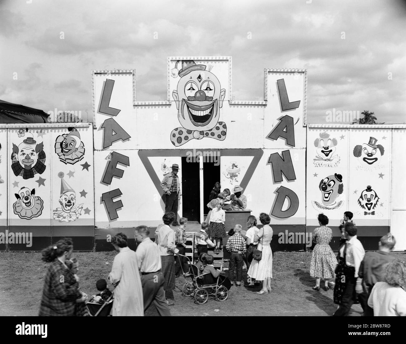 1950s LINE OF PEOPLE AT ENTRANCE TO FUNHOUSE BYING TICKETS AT LOCAL FAIR - f10060 HEL001 HARS ENTERTAINMENT B&W CLOWNS AMUSEMENT HIGH ANGLE ADVENTURE EXCITEMENT RECREATION LOCAL OCCUPATIONS FAIRS FUN HOUSE JUVENILES BLACK AND WHITE CAUCASIAN ETHNICITY OLD FASHIONED Stock Photo