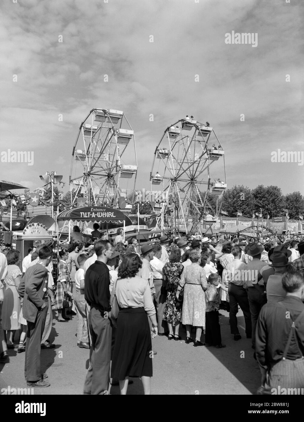 1940s 1950s CROWD AT LOCAL COUNTY FAIR CARNIVAL WITH 2 FERRIS WHEELS IN BACKGROUND - f3717 HEL001 HARS COUNTRY FAIR FAIRS AMUSEMENTS DAYLIGHT RIDES TOGETHERNESS BLACK AND WHITE CAUCASIAN ETHNICITY FERRIS WHEEL OLD FASHIONED Stock Photo
