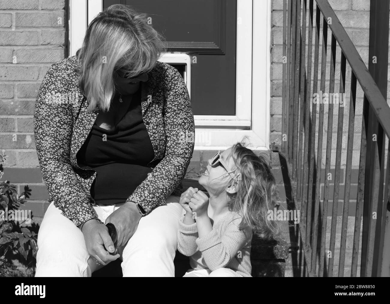 Lockdown doorstep portrait of Mother and daughter looking at each other. Black and white Stock Photo