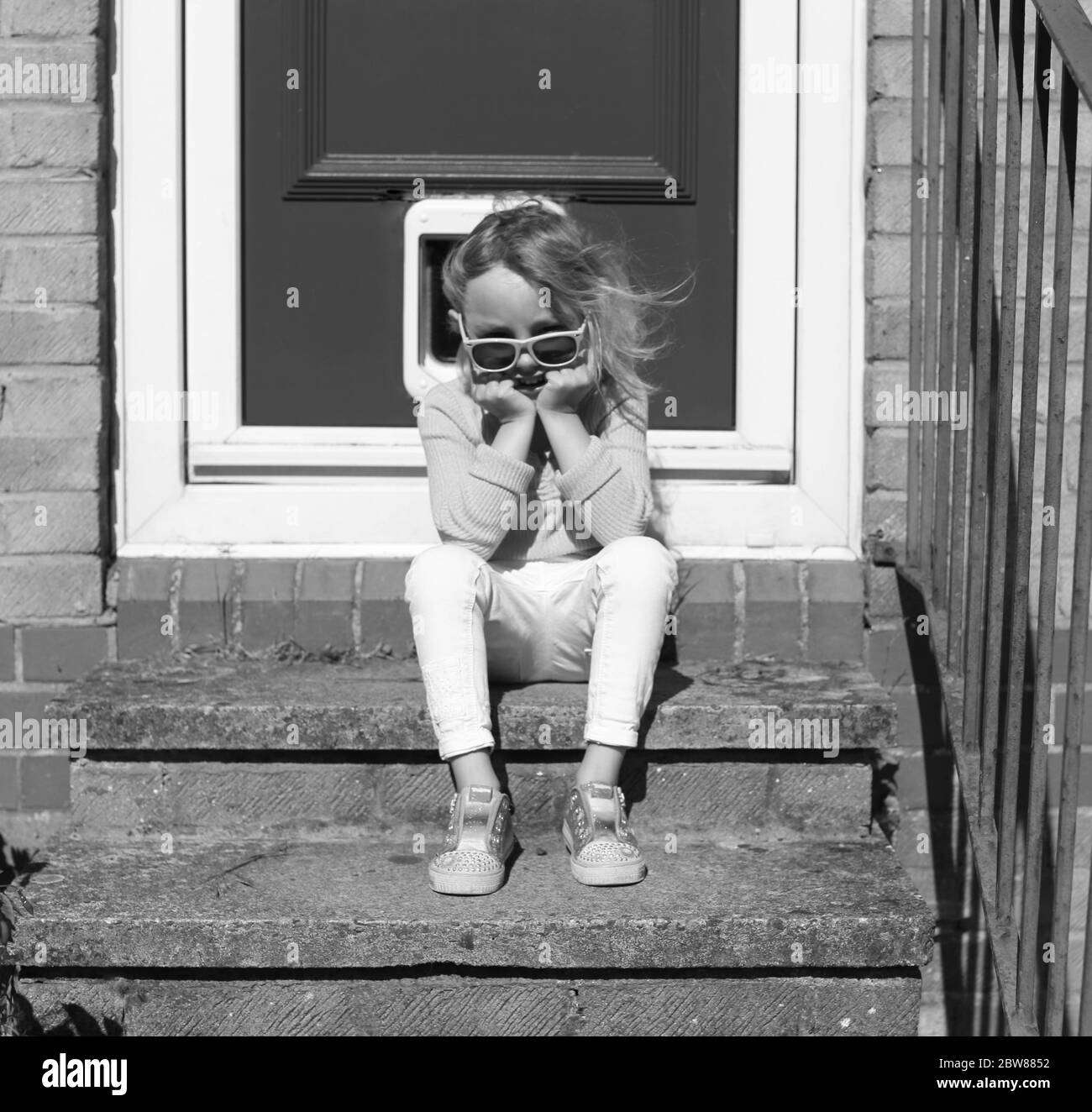 young child sat alone on doorstep. Lockdown portrait Stock Photo
