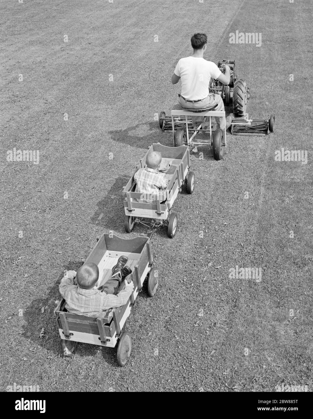 1950s 1960s MAN FATHER MOWING GRASS DRIVING RIDING LARGE LAWNMOWER TOWING TWO BOYS SONS BROTHERS EACH SITTING IN A WAGON  - g5633 HEL001 HARS 1 MOWER SILLY WAGON JUVENILE COMIC SAFETY TEAMWORK LAWNMOWER MOWING SONS JOY LIFESTYLE BROTHERS RURAL HOME LIFE COPY SPACE FULL-LENGTH PERSONS MALES RISK SIBLINGS TRANSPORTATION FATHERS B&W GOALS HUMOROUS HAPPINESS HIGH ANGLE CHORE STRATEGY DADS PROGRESS RECREATION COMICAL INNOVATION A IN OPPORTUNITY SIBLING CONNECTION TOWING YARD WORK CONCEPTUAL COMEDY IMAGINATION CREATIVITY GROWTH JUVENILES MID-ADULT MID-ADULT MAN RELAXATION SOLUTIONS TOGETHERNESS Stock Photo