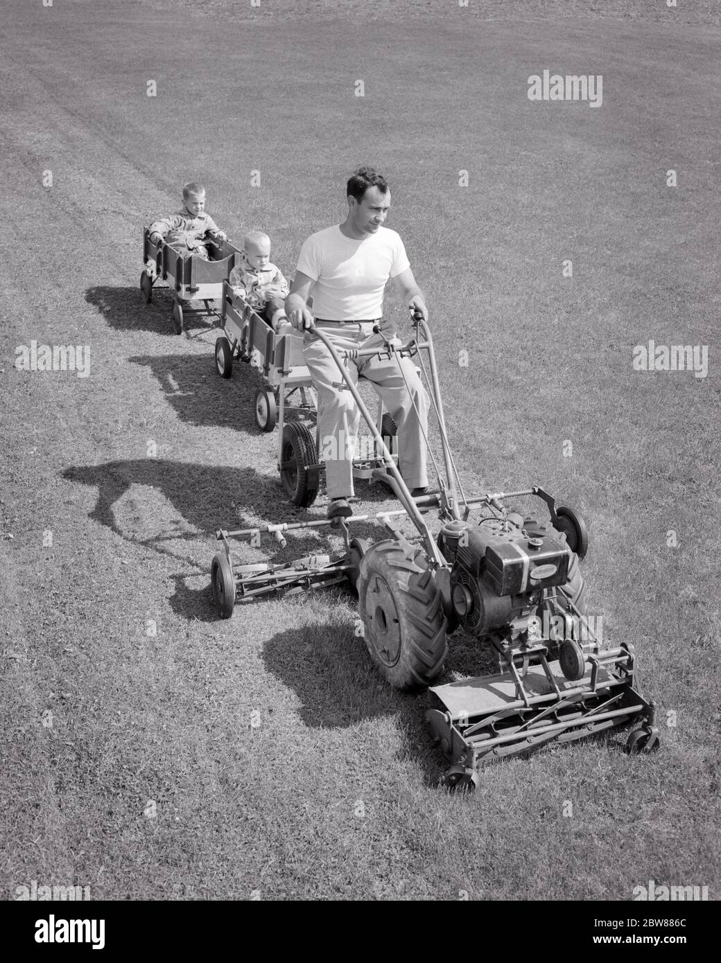 1950s-1960s-man-father-mowing-grass-driving-riding-large-lawnmower-towing-two-boys-sons-brothers-each-sitting-in-a-wagon-g5630-hel001-hars-old-fashion-1-mower-silly-wagon-juvenile-comic-safety-teamwork-lawnmower-mowing-sons-joy-lifestyle-brothers-rural-home-life-copy-space-full-length-persons-males-risk-siblings-transportation-fathers-bw-goals-humorous-happiness-high-angle-chore-strategy-dads-progress-recreation-comical-innovation-a-in-opportunity-sibling-using-connection-towing-yard-work-conceptual-lawn-mower-comedy-imagination-wagons-creativity-growth-juveniles-mid-adult-mid-adult-man-2BW886C.jpg