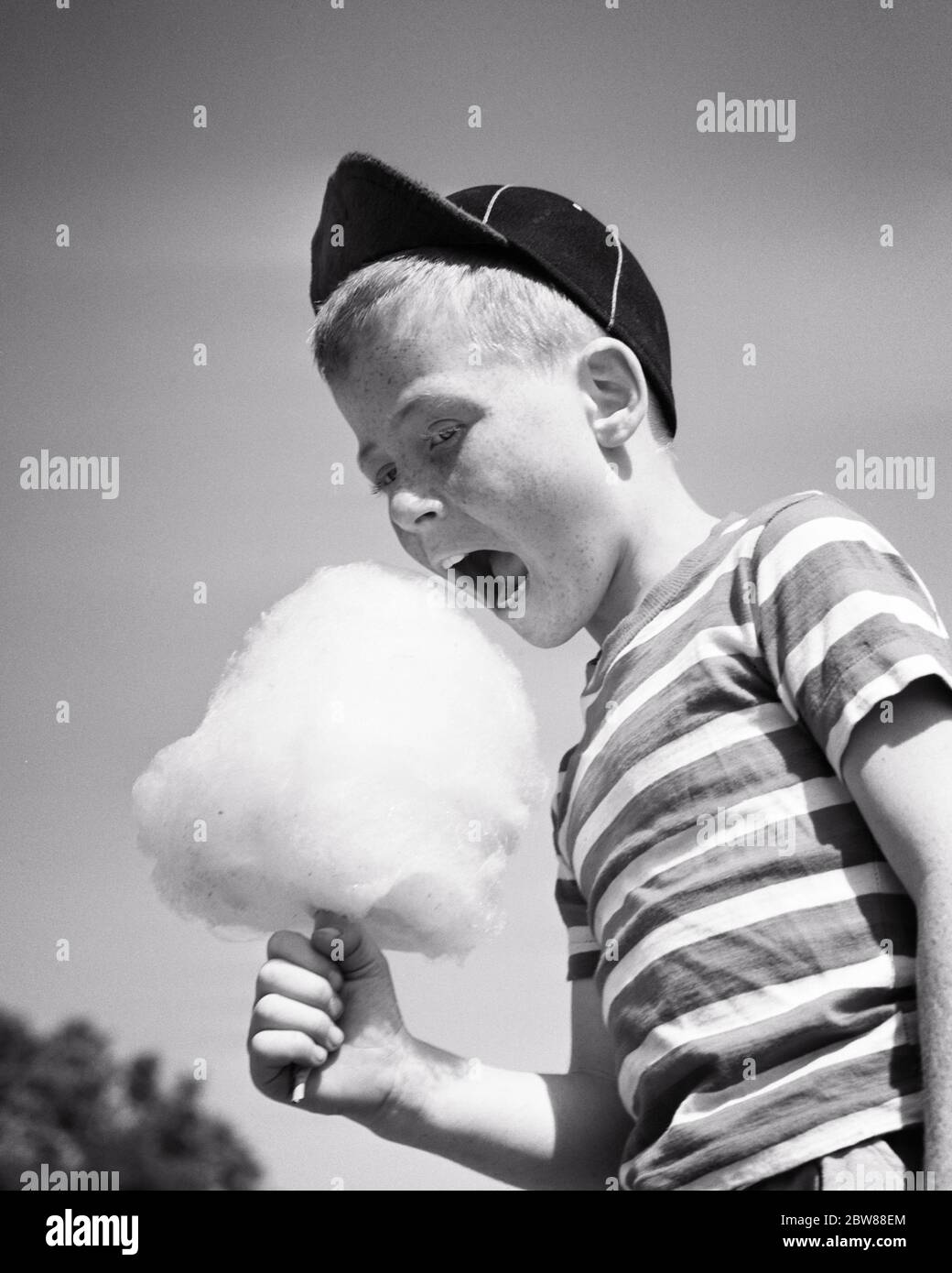 1950s BOY WEARING BASEBALL CAP AND STRIPED TEE SHIRT MOUTH WIDE OPEN EATING CARNIVAL COTTON CANDY TREAT - j2278 HEL001 HARS STRIPES SUGAR B&W SUMMERTIME PRETEEN BOY HAPPINESS AND EXCITEMENT LOW ANGLE OPEN MOUTH WIDE OPEN BITING STYLISH BASEBALL CAP COTTON CANDY JUVENILES PRE-TEEN PRE-TEEN BOY AMUSEMENT PARK BALL CAP BLACK AND WHITE CAUCASIAN ETHNICITY DELICIOUS MOUTH OPEN OLD FASHIONED Stock Photo