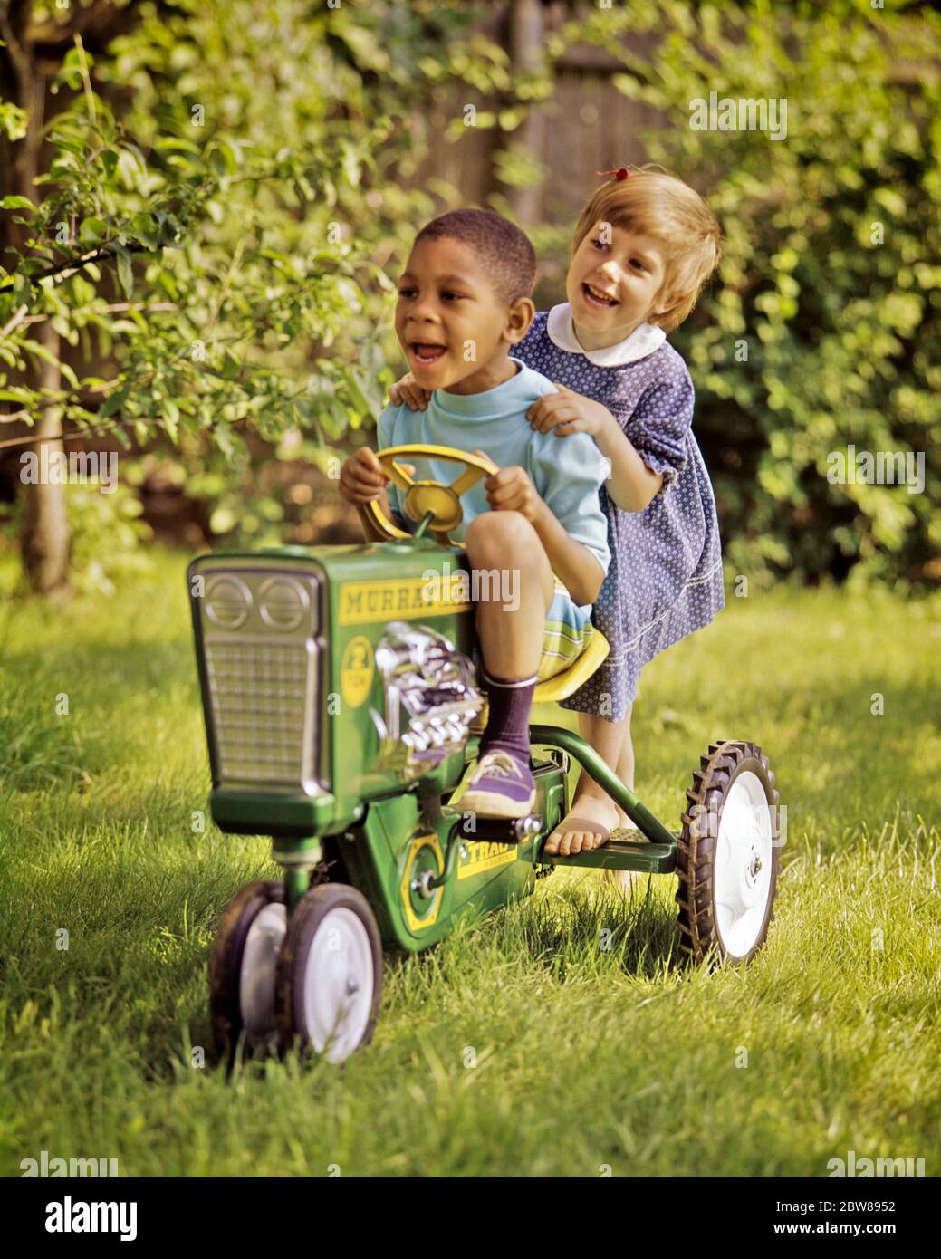 1960s AFRICAN-AMERICAN BOY DRIVING A TOY PEDDLE TRACTOR IN BACKYARD BAREFOOT CAUCASIAN GIRL HITCHING A RIDE ON BACK FOOT STEP - kj5460 PHT001 HARS 1 FOOT SILLY JUVENILE DIVERSE BLOND FRIEND COMIC TEAMWORK RIDE DIFFERENT JOY LIFESTYLE FEMALES TRACTOR RURAL HEALTHINESS HOME LIFE COPY SPACE FRIENDSHIP FULL-LENGTH HALF-LENGTH INSPIRATION MALES HUMOROUS HAPPINESS LEISURE AFRICAN-AMERICANS AFRICAN-AMERICAN AND LOW ANGLE BLACK ETHNICITY COMICAL A IN ON BAREFOOT CONNECTION PEDDLE CONCEPTUAL COMEDY FRIENDLY HITCHING VARIOUS VARIED COOPERATION JUVENILES TOGETHERNESS CAUCASIAN ETHNICITY OLD FASHIONED Stock Photo