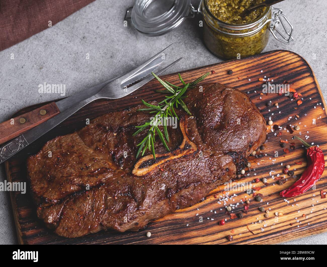 grilled beef steak with bone on a cutting board,  spices, sauce pesto Stock Photo