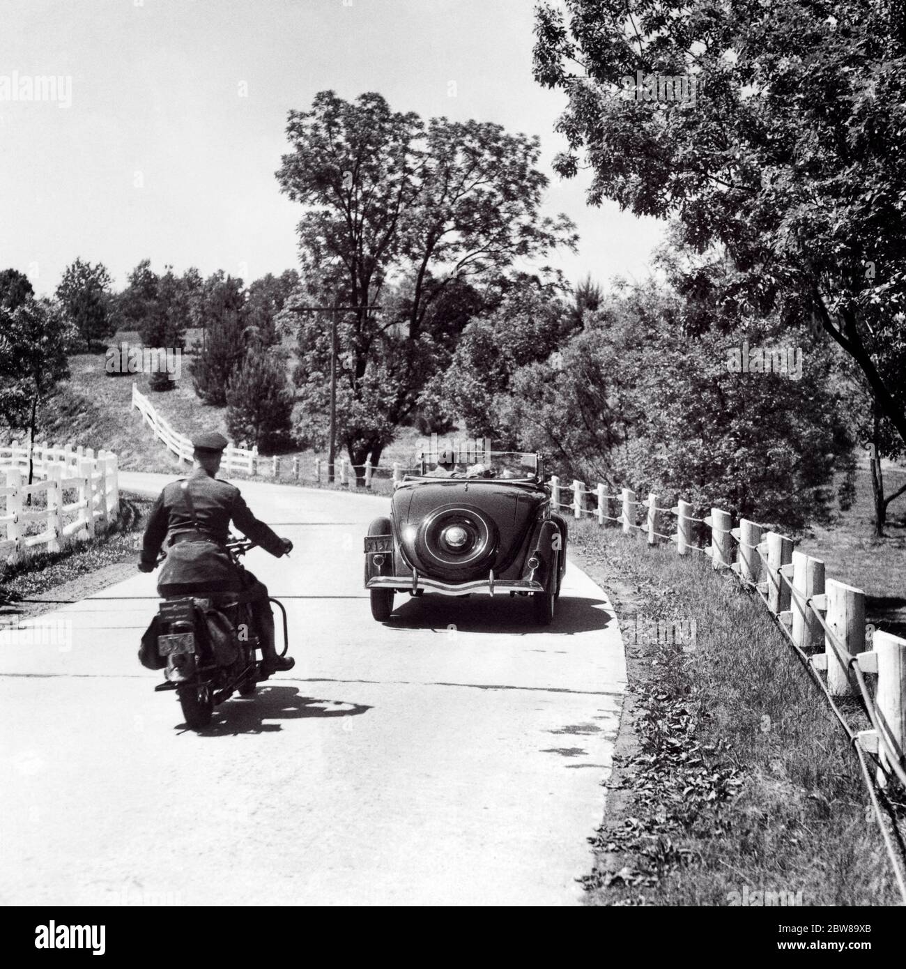 1930s 1940s MAN HIGHWAY PATROL POLICE OFFICER ON MOTORCYCLE PURSUING CONVERTIBLE CAR WITH COUPLE TWO PASSENGERS ON COUNTRY ROAD - m4762 HAR001 HARS POLICEMAN VEHICLE SAFETY LIFESTYLE SPEED FEMALES PASSENGERS RURAL COPY SPACE HALF-LENGTH HIGHWAY LADIES PERSONS AUTOMOBILE MALES RISK OFFICER TRANSPORTATION B&W COP PROTECT AND SERVE HIGH ANGLE ADVENTURE AUTOS EXCITEMENT REAR VIEW ON AUTHORITY OCCUPATIONS SPEEDING UNIFORMS PATROL CONCEPTUAL FROM BEHIND AUTOMOBILES VEHICLES OFFICERS POLICEMEN PURSUING BACK VIEW CHASING COOPERATION COPS TOGETHERNESS BADGE BADGES BLACK AND WHITE HAR001 OLD FASHIONED Stock Photo