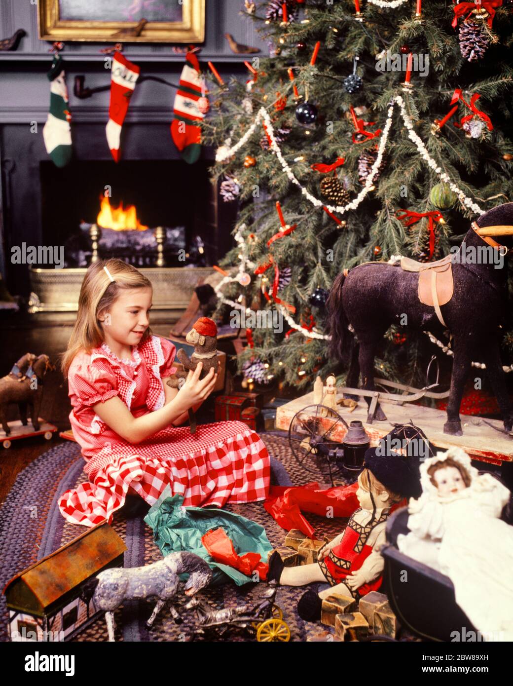 1970s 1980s BLOND GIRL HOLDING ANTIQUE TOY MONKEY BY TRADITIONAL CHRISTMAS TREE FIREPLACE ANTIQUE TOYS ALL AROUND TREE  - kx8812 PHT001 HARS SATISFACTION CELEBRATION FEMALES RURAL HEAT HOME LIFE COPY SPACE HALF-LENGTH INSPIRATION TRADITIONAL CARING DREAMS HAPPINESS DISCOVERY MERRY PORCELAIN EXCITEMENT MODELS TRADITION DECEMBER CONCEPTUAL DECEMBER 25 WARMTH ESTABLISHED STYLISH CHRISTMAS TREE COLLECTIBLES JOYOUS JUVENILES CAUCASIAN ETHNICITY COLLECTIBLE OLD FASHIONED RED AND WHITE Stock Photo