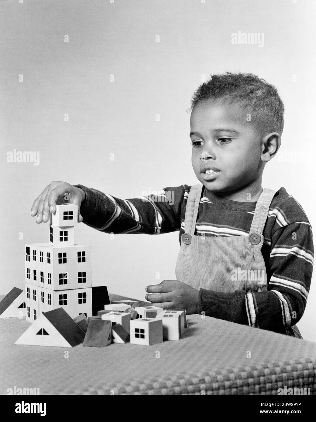 1950s ENGROSSED AFRICAN-AMERICAN BOY PLAYING BUILDING CONSTRUCTING APARTMENT HOUSE STRUCTURE WITH TOY ARCHITECTURAL BLOCKS - n633 HAR001 HARS COPY SPACE HALF-LENGTH MALES ARCHITECT CONFIDENCE EXPRESSIONS BUILDER B&W STRUCTURE ARCHITECTURAL DISCOVERY AFRICAN-AMERICANS AFRICAN-AMERICAN CHOICE THINK BLACK ETHNICITY OCCUPATIONS CONNECTION CONCEPTUAL IMAGINATION BIB OVERALLS T-SHIRT CREATIVITY FOCUSED GROWTH JUVENILES SOLUTIONS ATTENTIVE BLACK AND WHITE CONCENTRATING HAR001 OLD FASHIONED AFRICAN AMERICANS Stock Photo