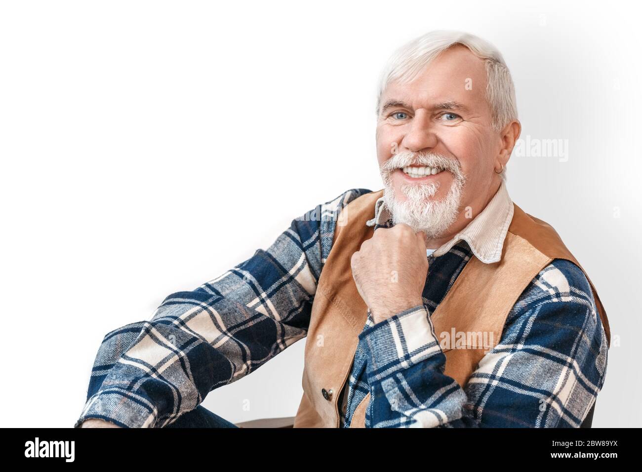 Freestyle. Senior bearded stylish man sitting isolated on white touching chin smiling joyful close-up Stock Photo