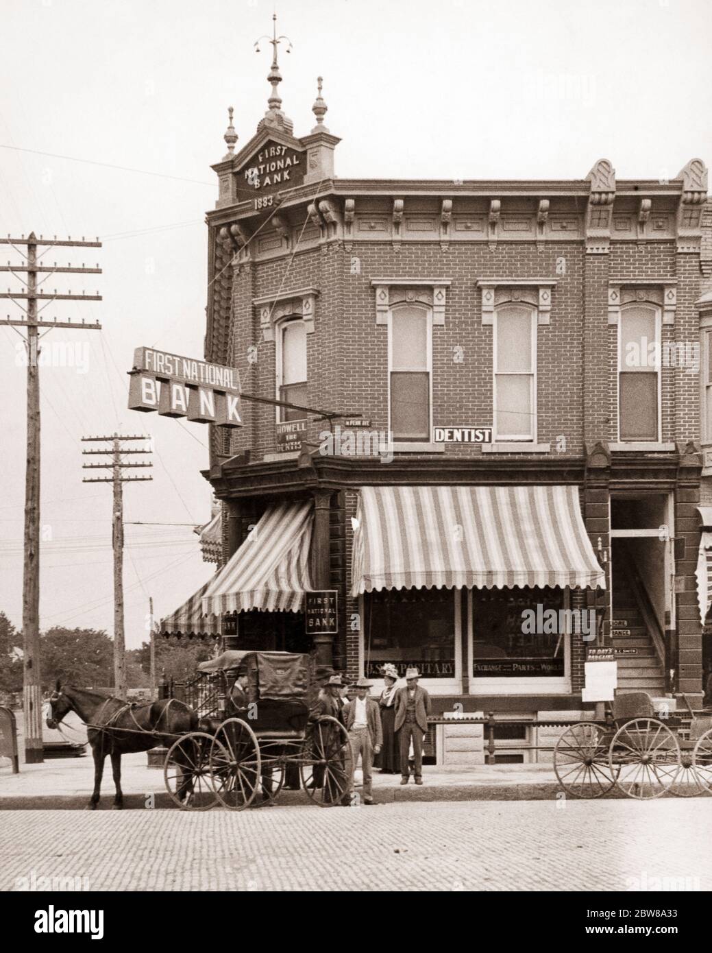 1910s PEOPLE HORSE & BUGGY IN FRONT OF FIRST NATIONAL BANK BUILDING WITH AWNINGS AND UPSTAIRS DENTIST INDEPENDENCE KANSAS USA - q49731 CPC001 HARS UNITED STATES OF AMERICA MALES CORNER KANSAS BUILDINGS WHEELS TRANSPORTATION B&W NORTH AMERICA NORTH AMERICAN MAMMALS NEIGHBORHOOD CANVAS PROPERTY KS CUSTOMER SERVICE AND CHOICE EXTERIOR INNOVATION OCCUPATIONS AWNINGS REAL ESTATE STRUCTURES UPSTAIRS WAGONS EDIFICE IN FRONT OF MAMMAL TWO STORY BLACK AND WHITE OLD FASHIONED Stock Photo