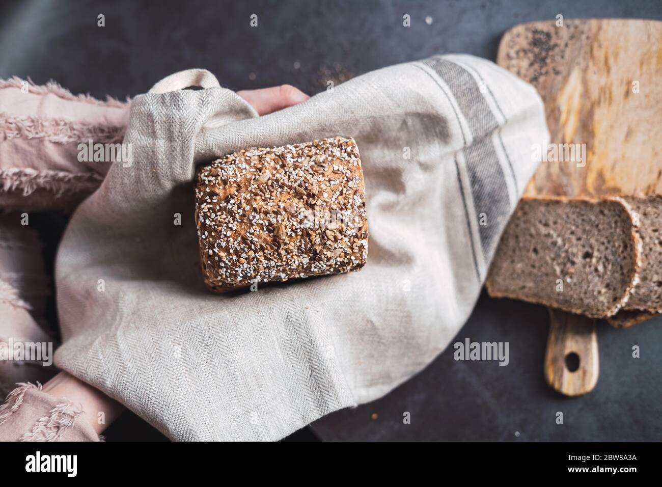 Hands holding a multi seed bread and some slices on the background. Stock Photo