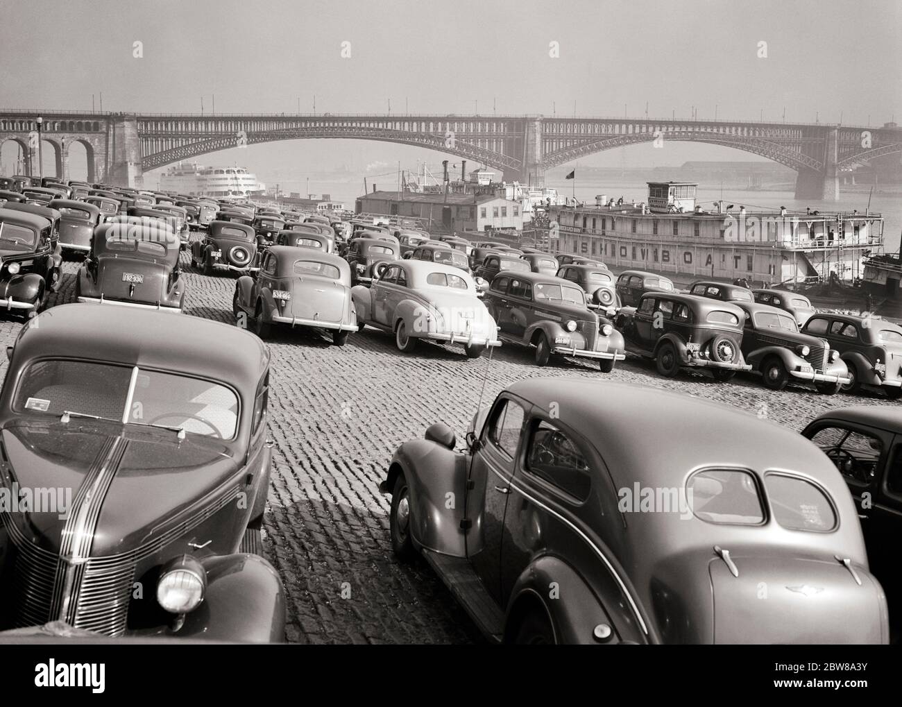 1930s 1940s CARS PARKED ON THE LEVEE LOT AND A SHOW BOAT AND SS ADMIRAL DOCKED ON THE MISSISSIPPI RIVER ST. LOUIS MISSOURI  - r1885 HAR001 HARS WIDE ANGLE HIGH ANGLE LOUIS AND AUTOS EXCITEMENT MISSOURI PROGRESS RECREATION STEAM POWERED AT ON OCCUPATIONS CONCEPTUAL DOCKED AUTOMOBILES ST. VEHICLES LEVEE SS SS ADMIRAL TOWBOAT ADMIRAL BLACK AND WHITE HAR001 MIDWEST MIDWESTERN MISSISSIPPI MISSISSIPPI RIVER MO MOORED OLD FASHIONED PADDLE WHEEL ST. LOUIS Stock Photo