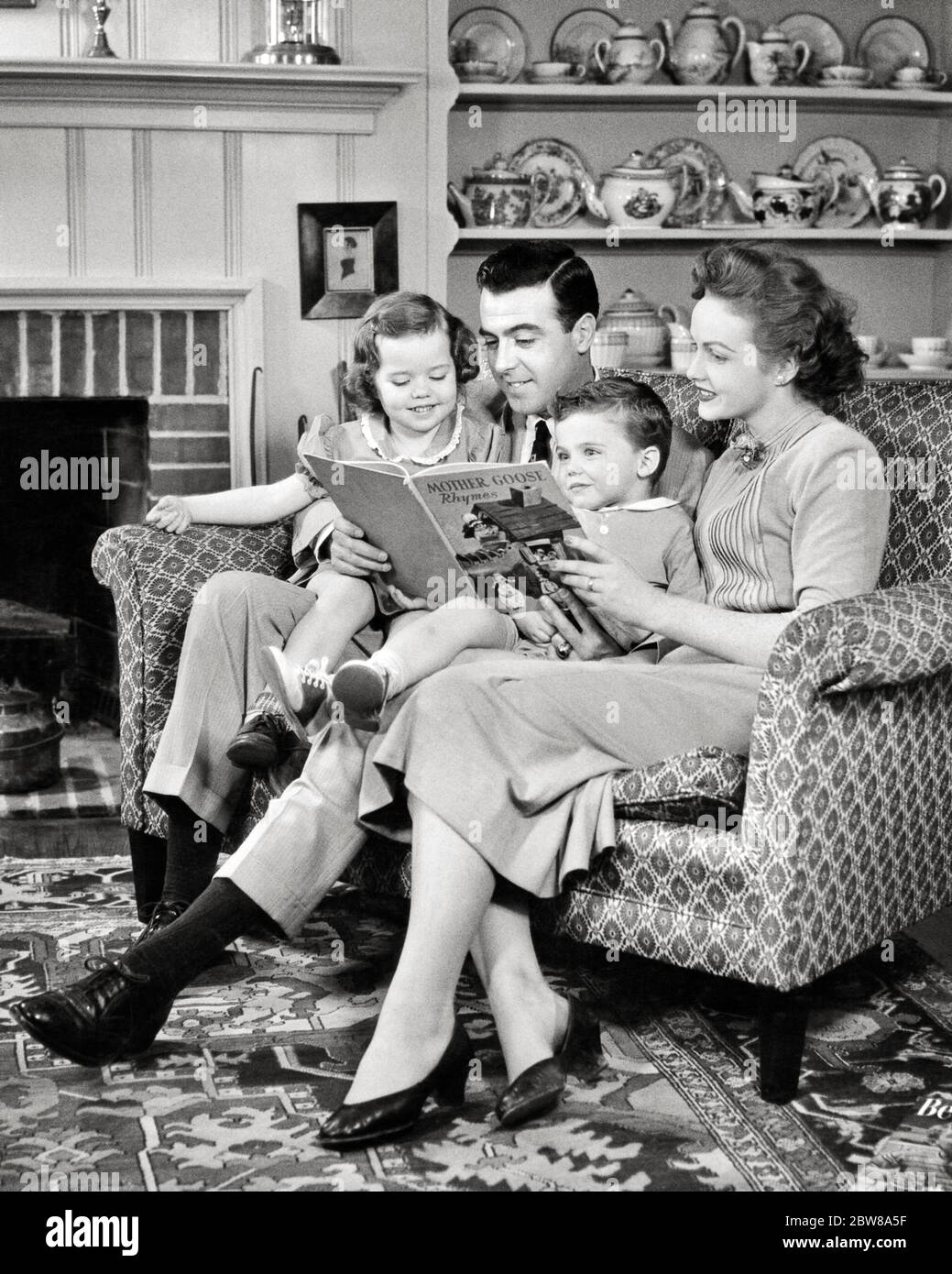 1950s FAMILY SITTING TOGETHER ON SOFA READING MOTHER GOOSE BOOK MOTHER FATHER YOUNG BOY AND GIRL - r4801 HAR001 HARS NOSTALGIA BROTHER OLD FASHION SISTER JUVENILE COMMUNICATION YOUNG ADULT SONS FAMILIES LIFESTYLE SATISFACTION FEMALES BROTHERS HEALTHINESS HOME LIFE COPY SPACE FRIENDSHIP HALF-LENGTH LADIES DAUGHTERS PERSONS INSPIRATION TRADITIONAL MALES SIBLINGS SISTERS FATHERS B&W HAPPINESS AND DADS SIBLING CONNECTION CONCEPTUAL STYLISH MIDDLE CLASS BABY BOY MOTHER GOOSE COOPERATION JUVENILES MOMS TOGETHERNESS YOUNG ADULT MAN YOUNG ADULT WOMAN BLACK AND WHITE CAUCASIAN ETHNICITY HAR001 Stock Photo
