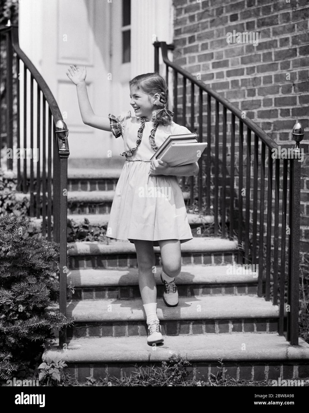 1940s SMILING GIRL WALKING DOWN STAIRS OF BRICK HOME CARRYING SCHOOL BOOKS  WAVING HER HAND WEARING BRAIDS SADDLE OXFORD SHOES - s3560 HEL001 HARS  STYLE COMMUNICATION INFORMATION PLEASED JOY LIFESTYLE SATISFACTION BRICK