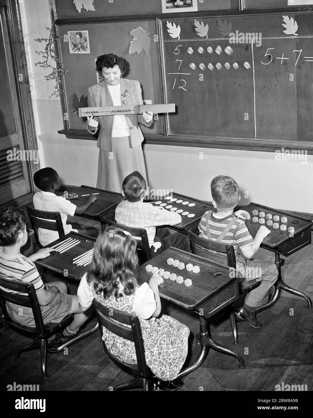 1950s ANONYMOUS WOMAN TEACHER AND SIX ELEMENTARY STUDENTS IN A MATH ARITHMETIC CLASS AT A SEEING AND HARD OF HEARING SCHOOL   - s3984 HAR001 HARS INFORMATION LIFESTYLE FEMALES 6 COPY SPACE HALF-LENGTH MALES SIX B&W GOALS SCHOOLS VISION GRADE HIGH ANGLE DISCOVERY AFRICAN-AMERICANS AFRICAN-AMERICAN INSTRUCTOR KNOWLEDGE BLACK ETHNICITY REAR VIEW SENSES OPPORTUNITY SEEING OCCUPATIONS PRIMARY VISUAL AID CONNECTION FROM BEHIND ADDITION ARITHMETIC EDUCATOR HEARING SIGHT BACK VIEW COOPERATION EDUCATING EDUCATORS GRADE SCHOOL INSTRUCTORS JUVENILES MID-ADULT MID-ADULT WOMAN SCHOOL TEACHES TACTILE Stock Photo