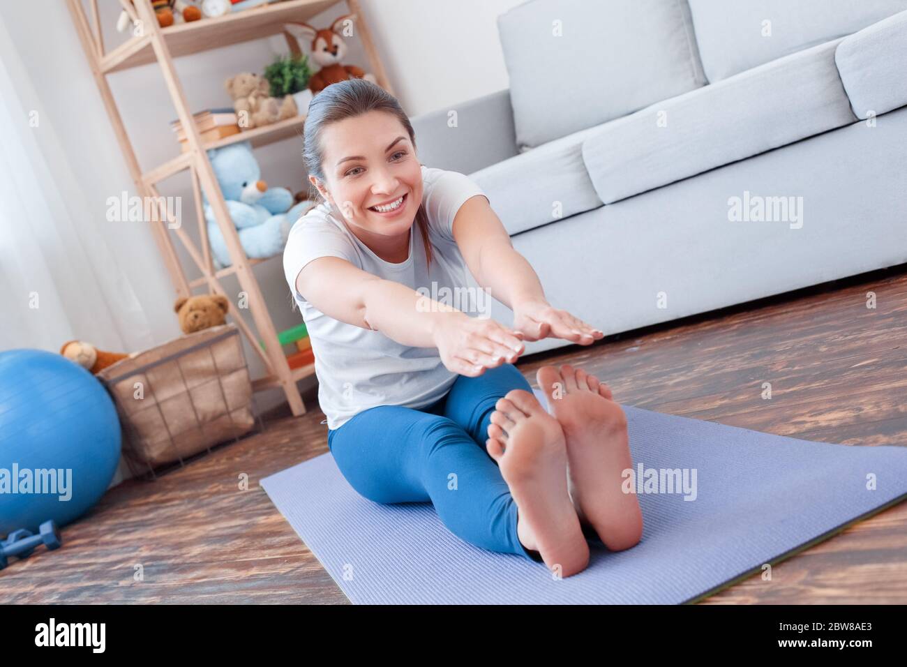 Healthy Lifestyle. Young woman doing yoga at home sitting legs apart bending down stretching smiling joyful Stock Photo
