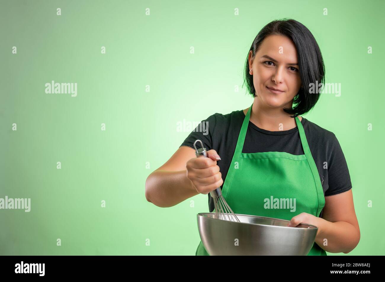 https://c8.alamy.com/comp/2BW8AEJ/female-cook-with-green-apron-and-black-t-shirt-hold-the-bowl-and-whisk-in-her-hands-isolated-on-green-background-2BW8AEJ.jpg