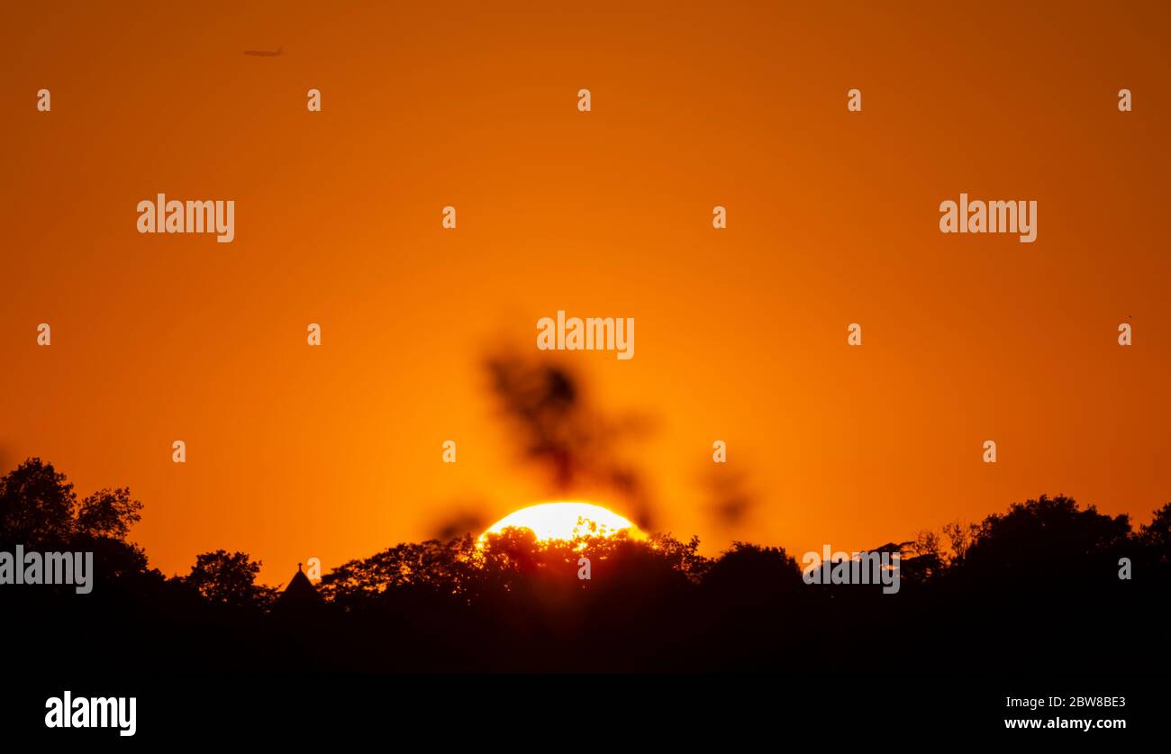 Wimbledon, London, UK. 30 May 2020. Spectacular orange sunset behind Wimbledon Hill on day 68 of Coronavirus lockdown with a departing aircraft from Heathrow. Credit: Malcolm Park/Alamy Live News. Stock Photo