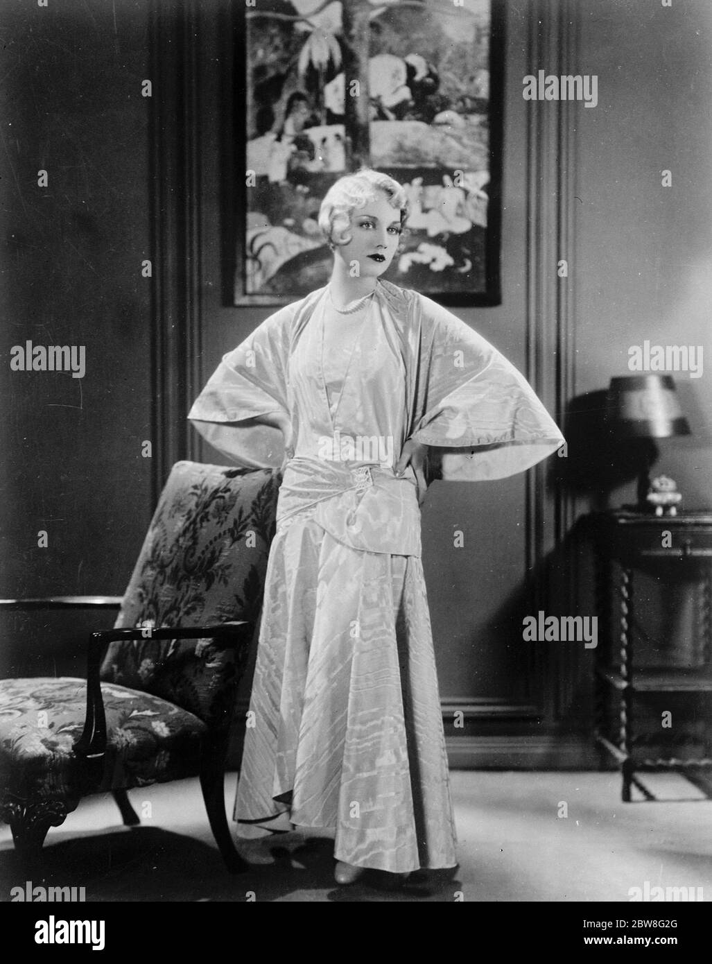 Unusual evening frock worn with smart cape coat of same material . Moire treated in an unusual manner for evening worn by Miss Leila Hyams . 3 May 1930 Stock Photo