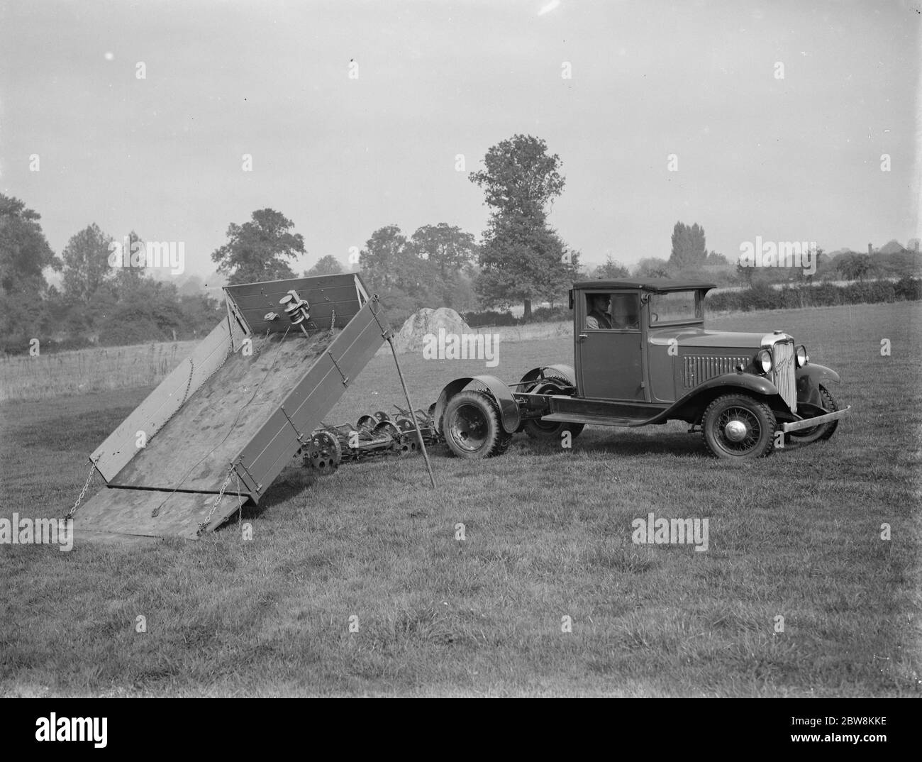 The empty trailer with the mower unloaded and now attached to the back of the truck ready for grass cutting . 1937 Stock Photo
