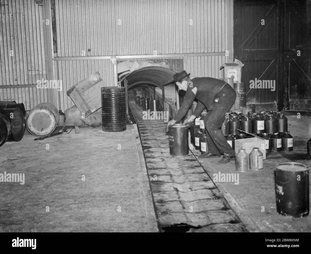 The Dussek Brothers and Co ltd , coal tar barrels are taken off the conveyor belt by a workman . 1938 Stock Photo