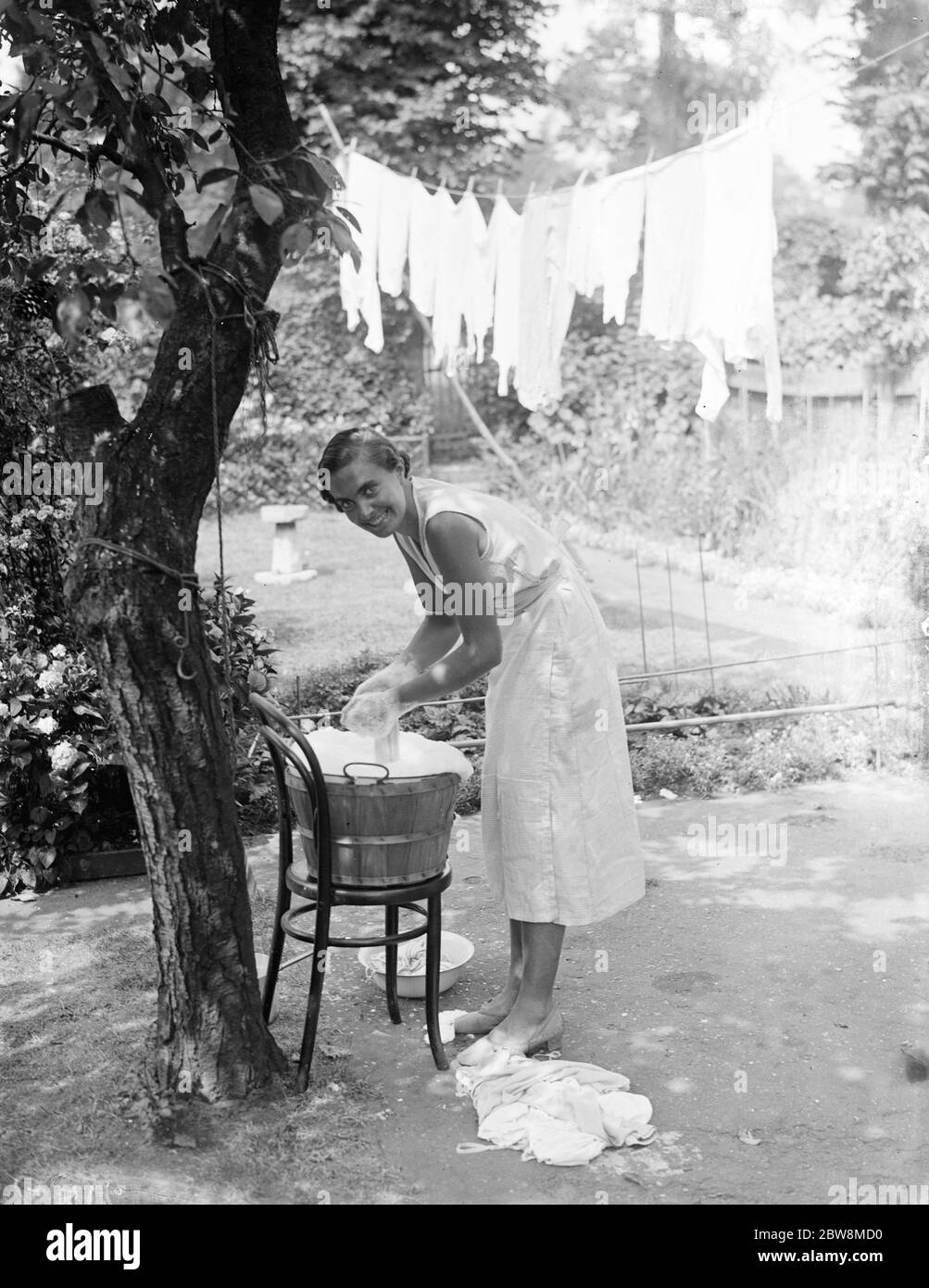 Washing day ; A smiling young housewife doing the washing in a tin bath and then hanging the clothes out on the washing line . 1935 Stock Photo
