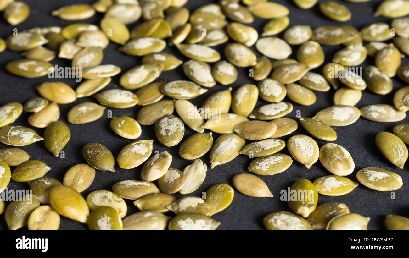 Scattered peeled pumpkin seeds as background. Top view of macro background texture of green pumpkin seeds Stock Photo