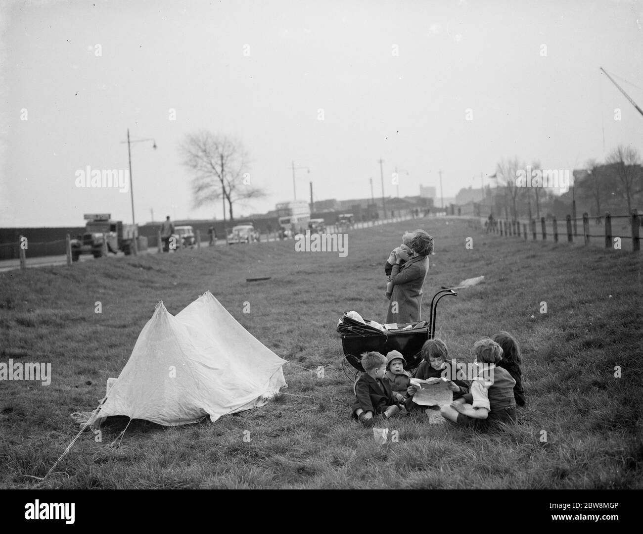 Children have a picnic on a bit of grass next to the road . 1938 Stock Photo