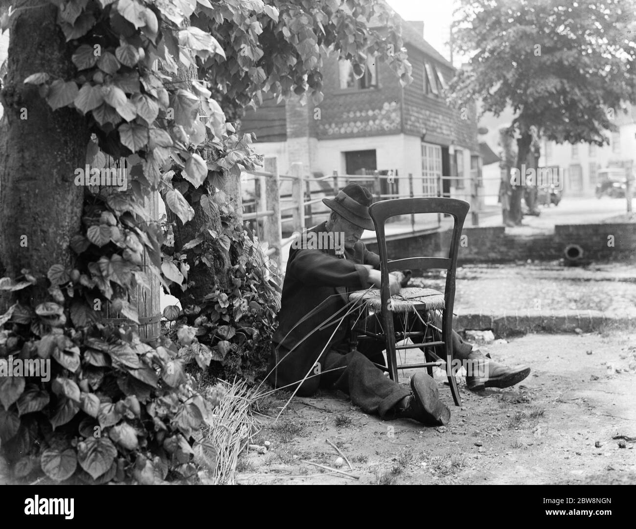 An elderly man fixes the seat of a chair with wicker . 1936 Stock Photo