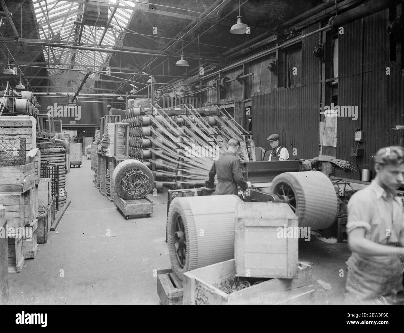 The Lloyd Loom loom that could weave twisted craft paper into a woven fabric, partly reinforced with steel wire. The loom in action in the foreground can be seen giant rolls of woven fibre, fresh from the loom, waiting to be taken to the cutting room. 1938 Stock Photo