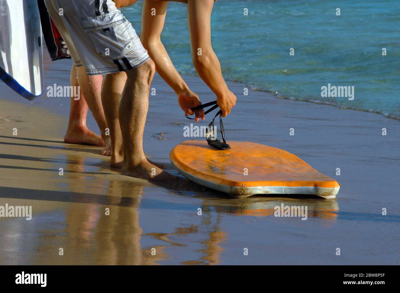 Boogie Boarder prepares to ride the waves.  He and buddies share the use of the orange boogie board. Stock Photo