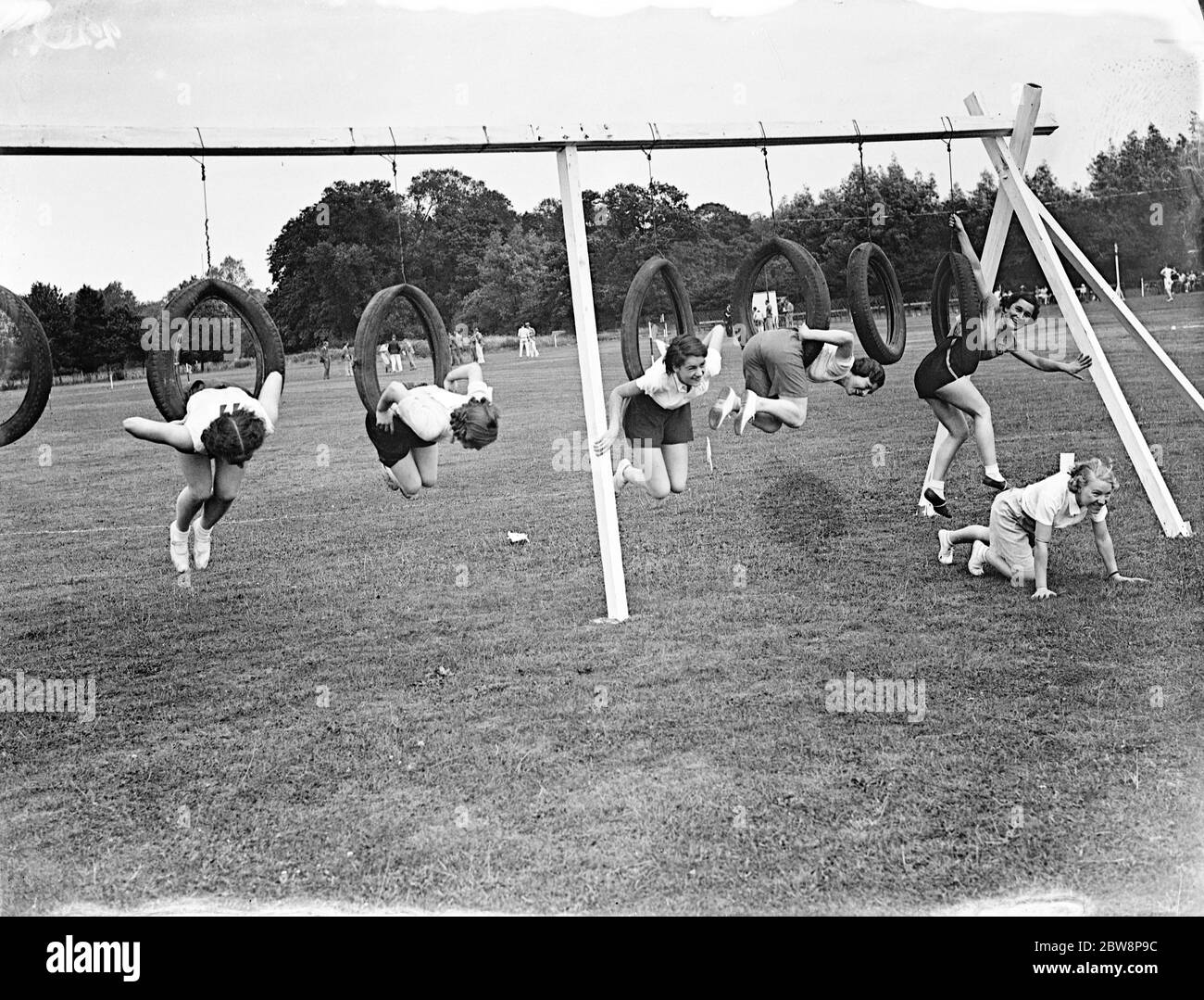 Girls climbing through tyres during a race at their sports day . 1935 Stock Photo