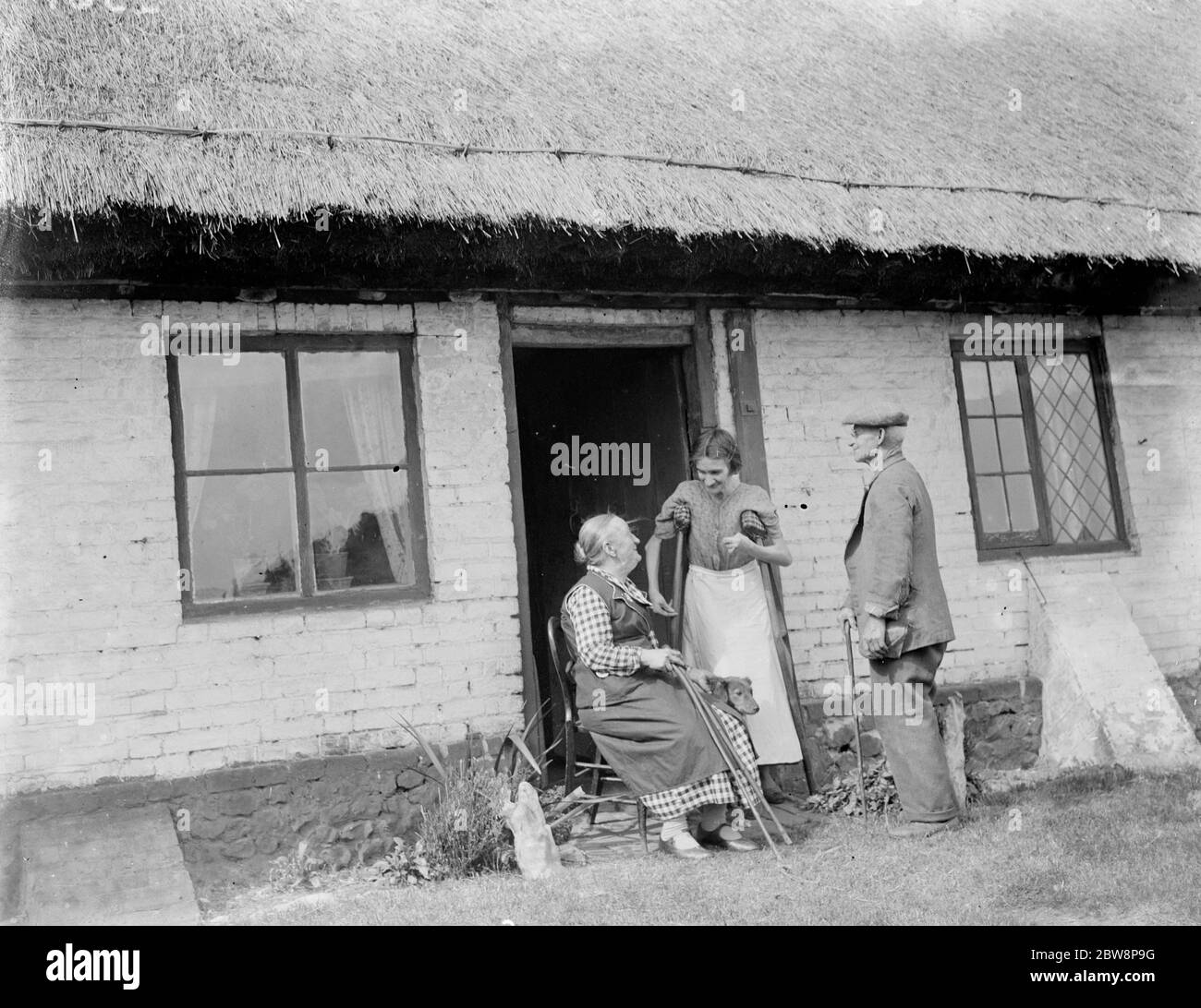 The elderly inhabitants of the thatched cottages in Bredgar , Kent , sitting outside their front doors . 1935 Stock Photo