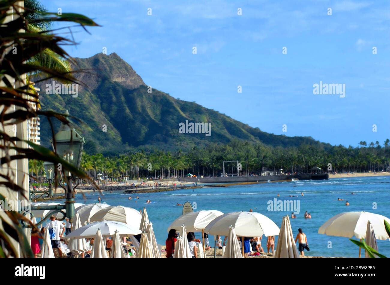 Hotel and umbrellas frame Diamond Head and Waikiki beach.  Crowded with bathers, swimmers and observers. Stock Photo