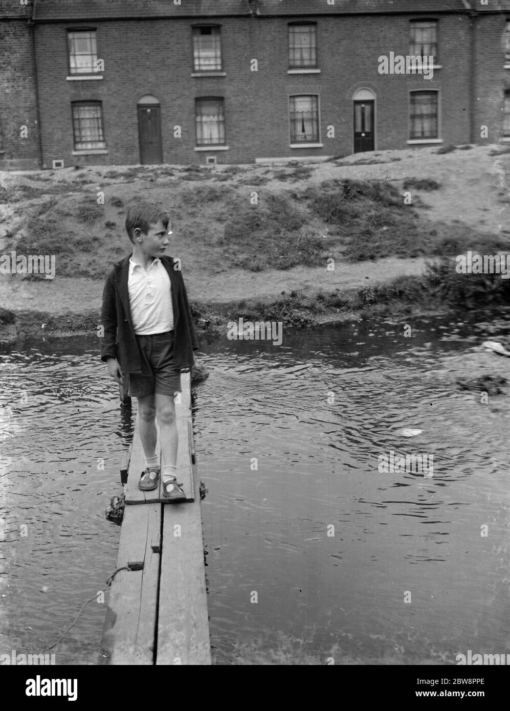 Mill road . A child crosses the stream on a scratch bridge . 1938 Stock Photo