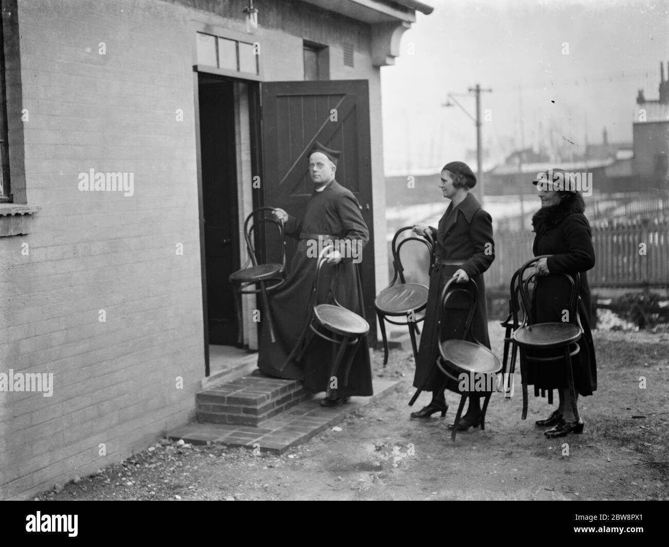 The Reverend M Cox moving chairs with some of his parishioners in Swanscombe , Kent . 1937 Stock Photo