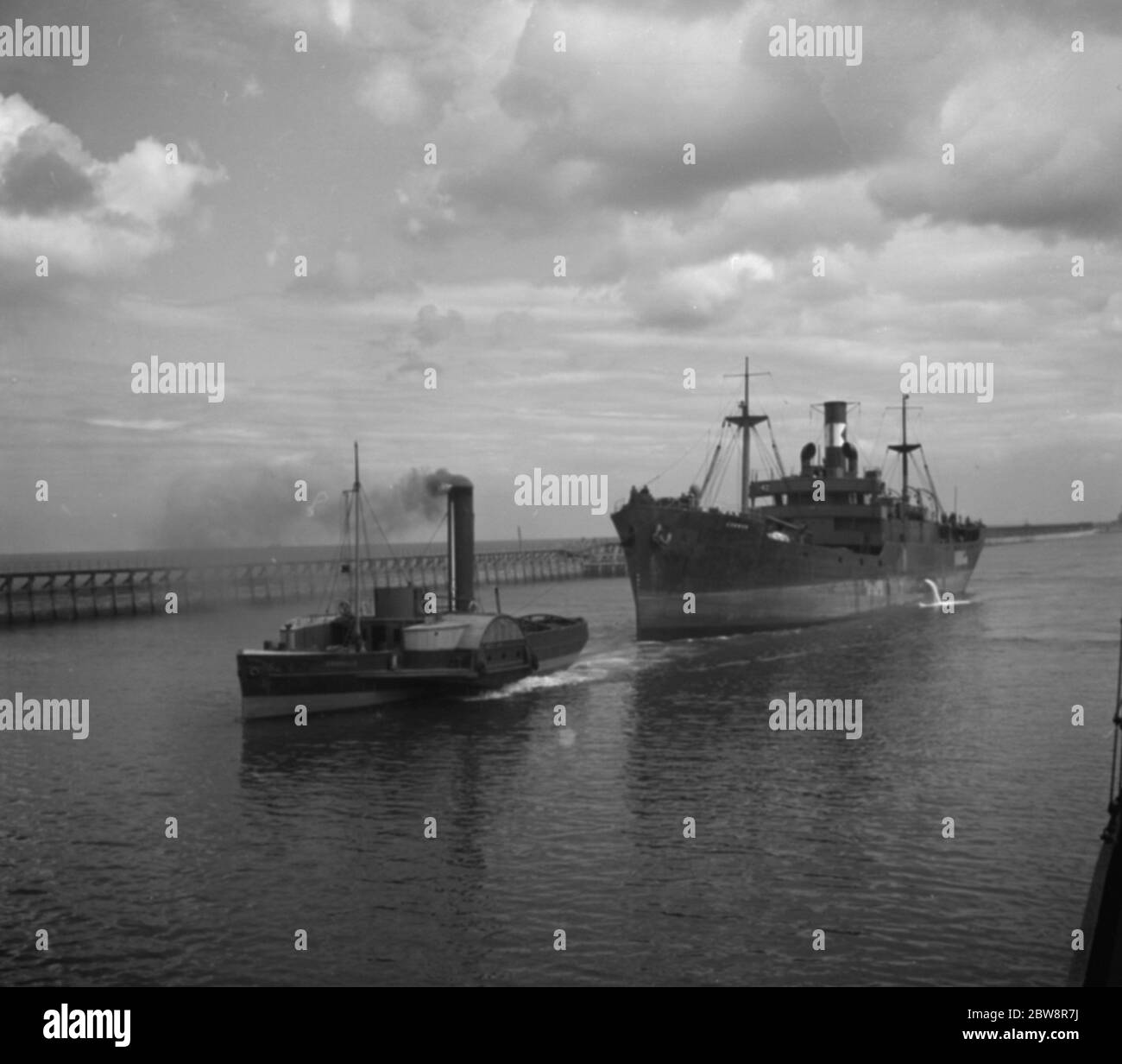 Merchant ship under tow from a paddle steamer tug . 1936 Stock Photo