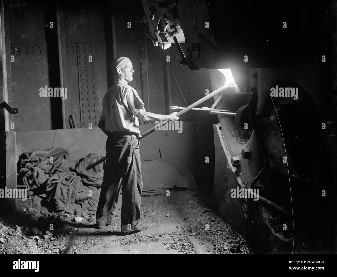 The stoker of the tramp steamer , ' SS Eston ' shovelling coal into the ship ' s boiler . 1935 Stock Photo