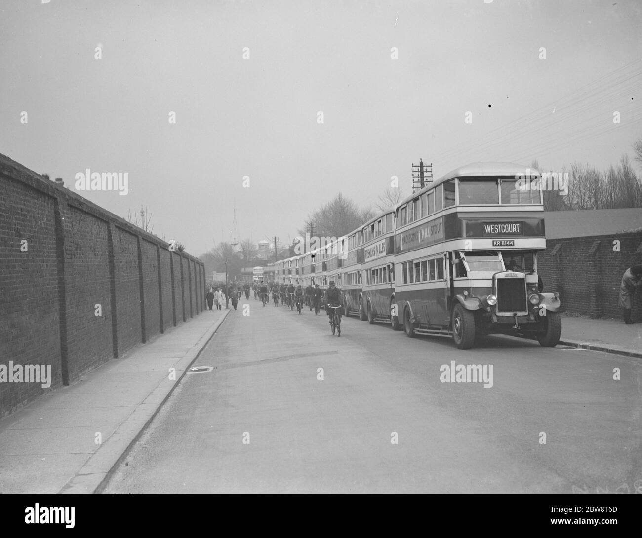 Buses parked on the road outside Chatham dockyard . Dock workers cycling past . 1938 Stock Photo