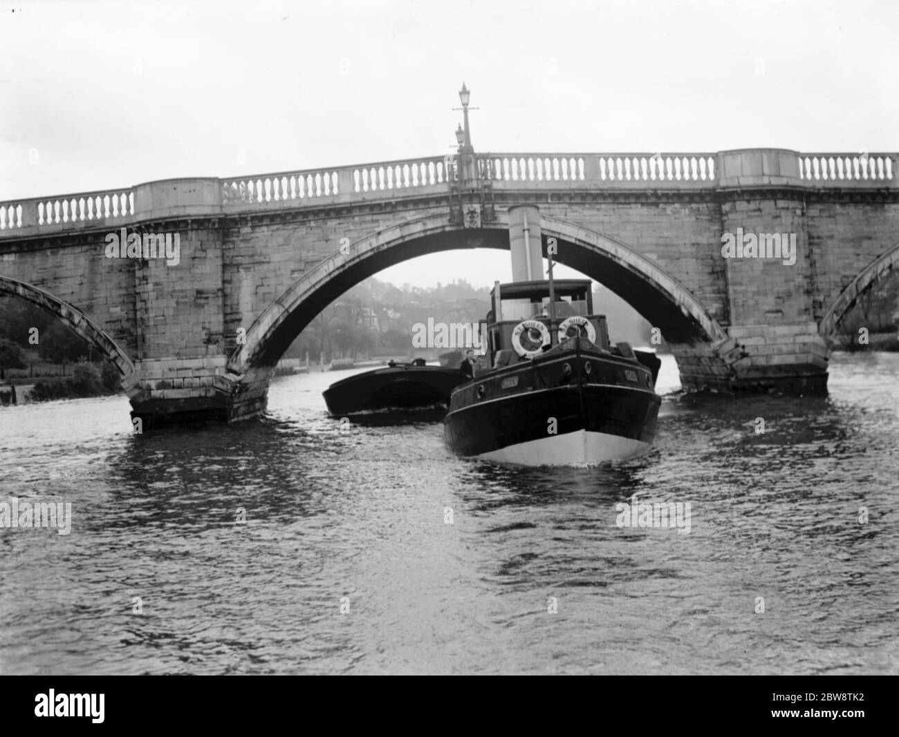Association of Master Lightermen and Barge Owners have placed an applications for the repair of Richmond Bridge on the river Thames in London . Photos shows a tug towing a laden barge under the Richmond Bridge . 1936 26 October 1936 Stock Photo