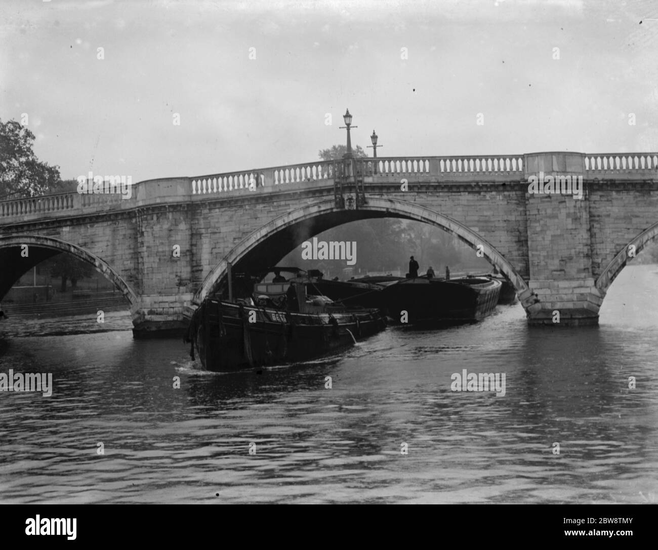 Association of Master Lightermen and Barge Owners have placed an applications for the repair of Richmond Bridge on the river Thames in London . Photos shows a tug towing a barge under the Richmond Bridge . 1936 26 October 1936 Stock Photo