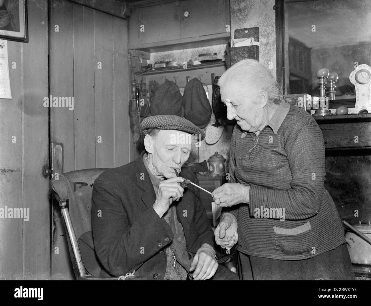 Mrs Hoskins using a match to light Mr Hoskins smoking pipe . 1938 . Stock Photo