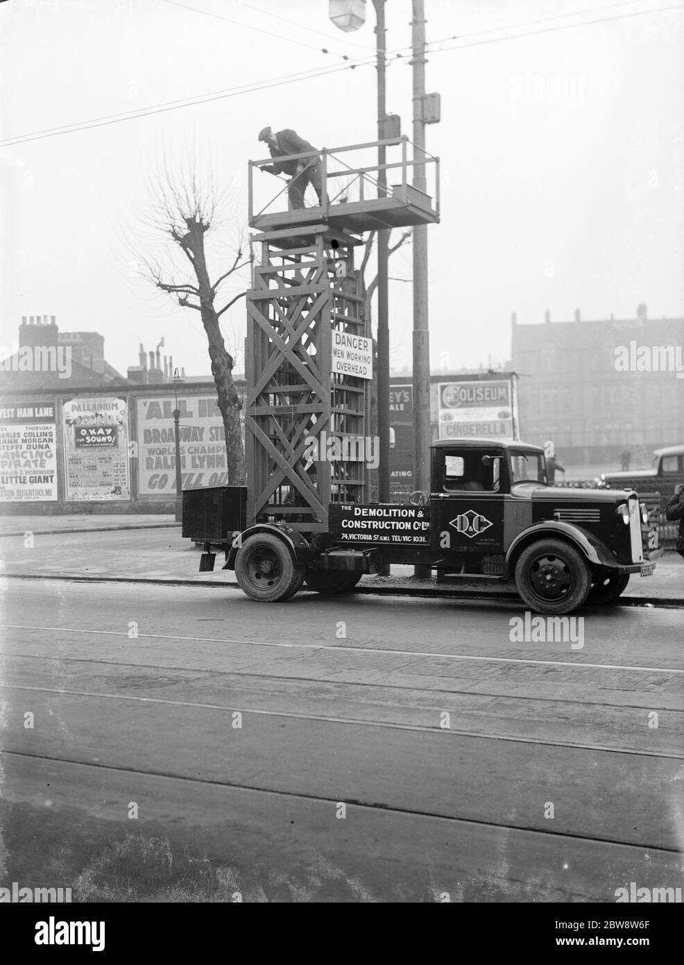 Workers from the Demolition and Construction Company Ltd use their Bedford Tram Tower truck to work on the overhead street lights . 1936 . Stock Photo