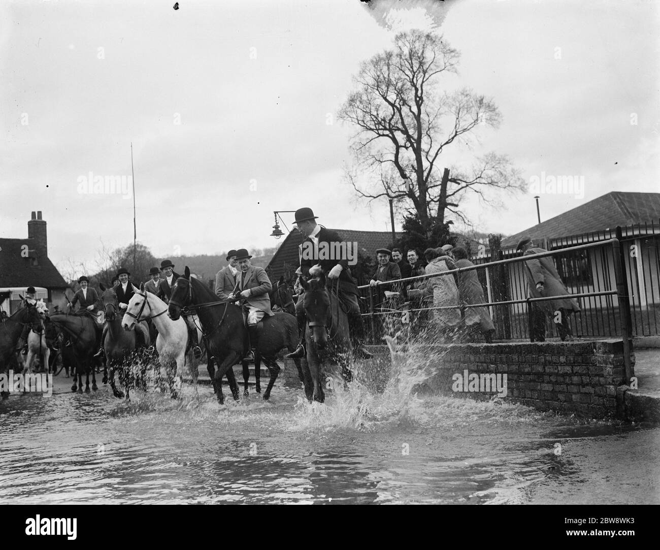 The Royal Artillery Drag Hunt cross a flooded street in Eynsford , Kent . 1937 Stock Photo