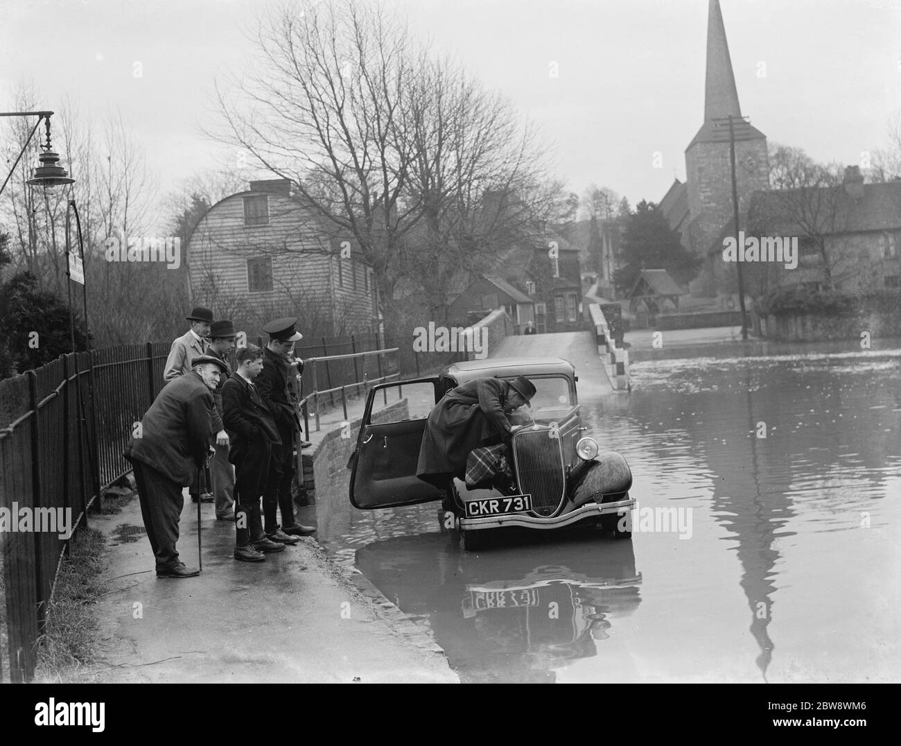 Flood in Eynsford . Passersby look on as a motorist tends to his flooded engine . 1937 Stock Photo