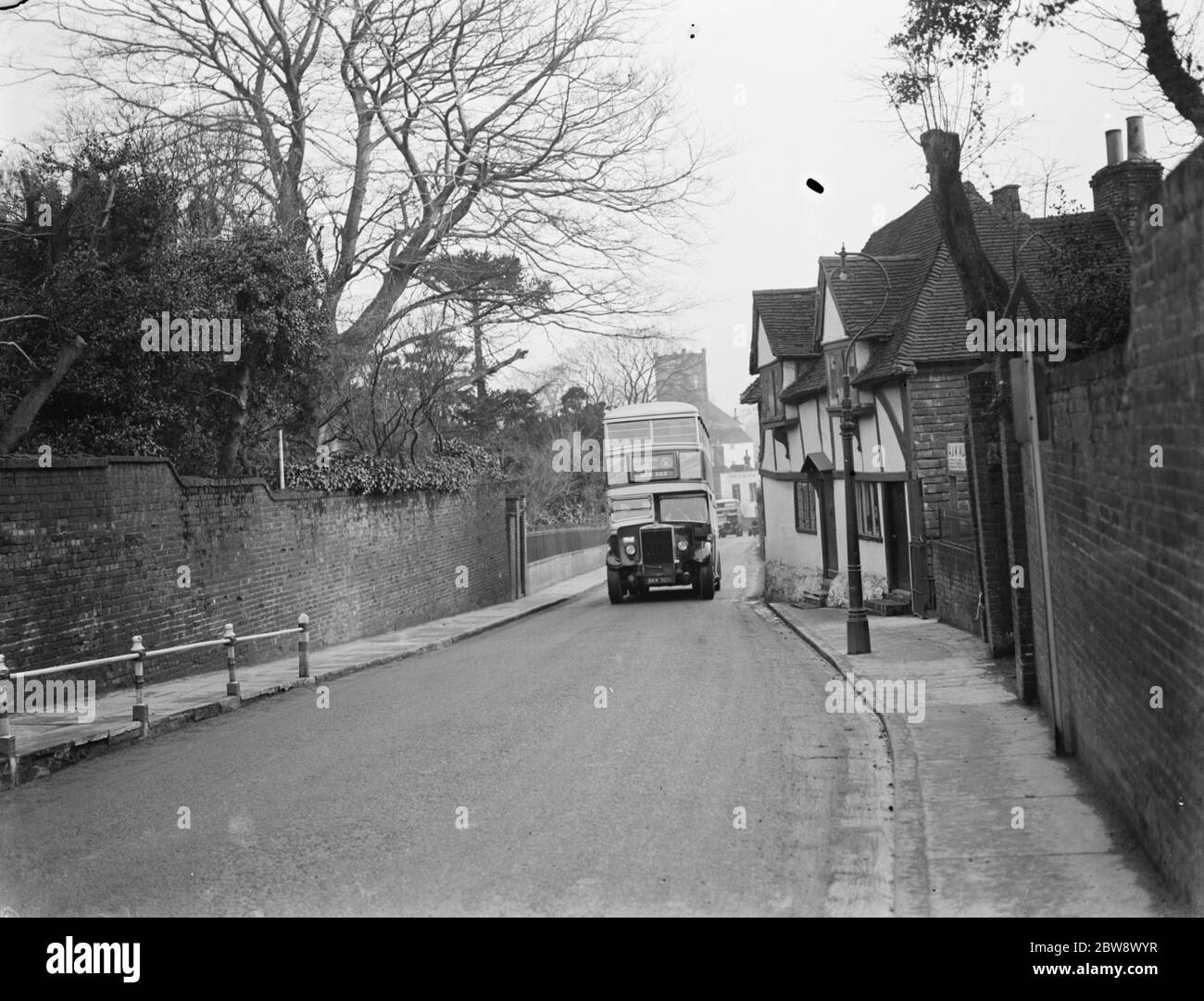 A double decker bus driving past some old cottages on a street in Ashford , Kent . 11 January 1939 Stock Photo