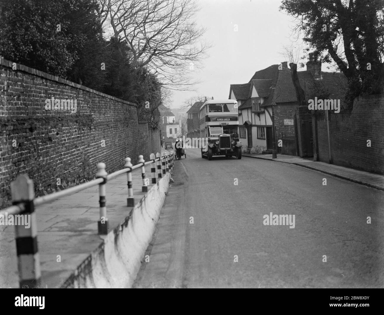 A double decker bus driving past some old cottages on a street in Ashford , Kent . 11 January 1939 Stock Photo