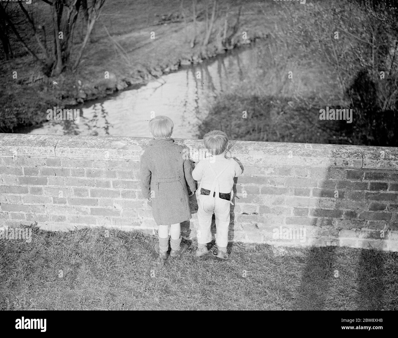 Back view of two little boys peering over a bridge . 1938 Stock Photo