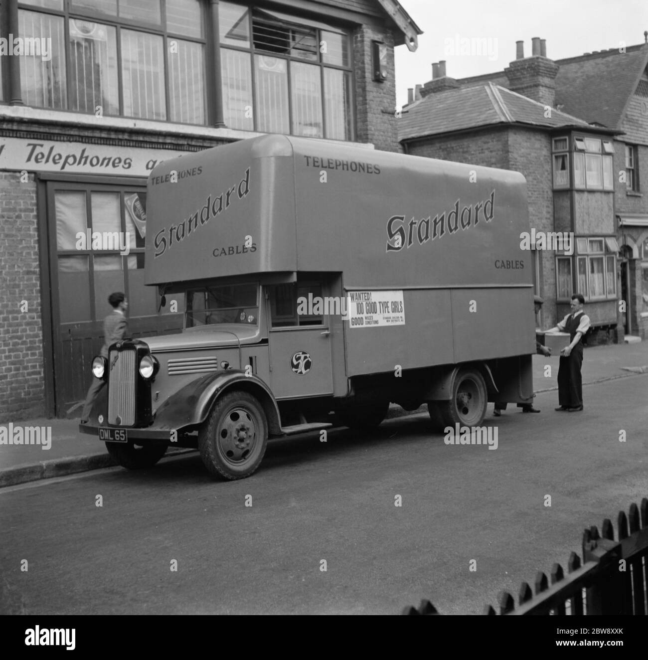 A worker loads boxes into a Bedford truck belonging to the Standard Telephone and Cables Company Ltd , parked outside their store . 1936 . Stock Photo