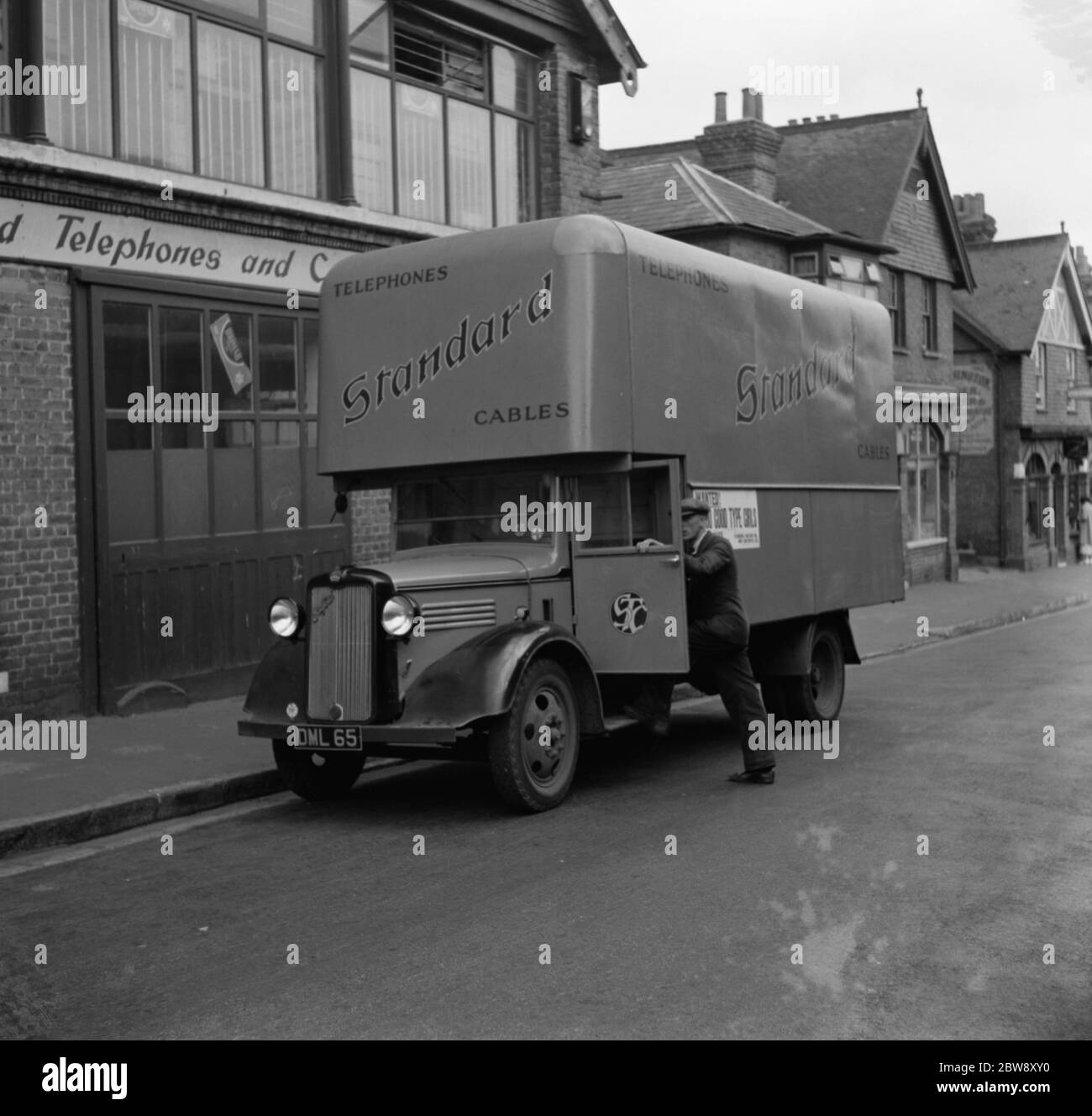 The driver climbs into the Bedford truck belonging to the Standard Telephone and Cables Company Ltd , parked outside their store . 1936 . Stock Photo